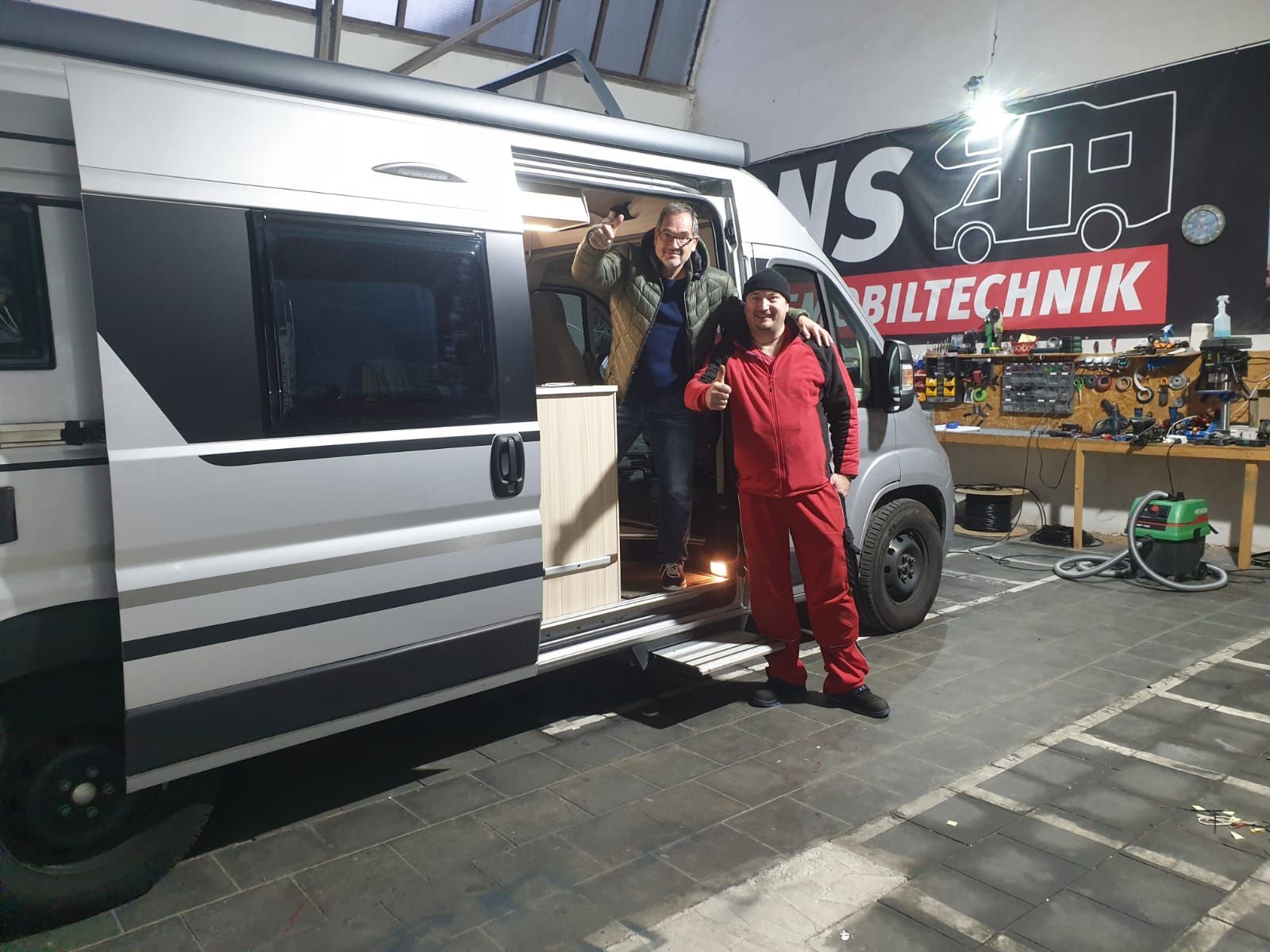 Zwei Männer stehen neben einem Lieferwagen in einer Garage.