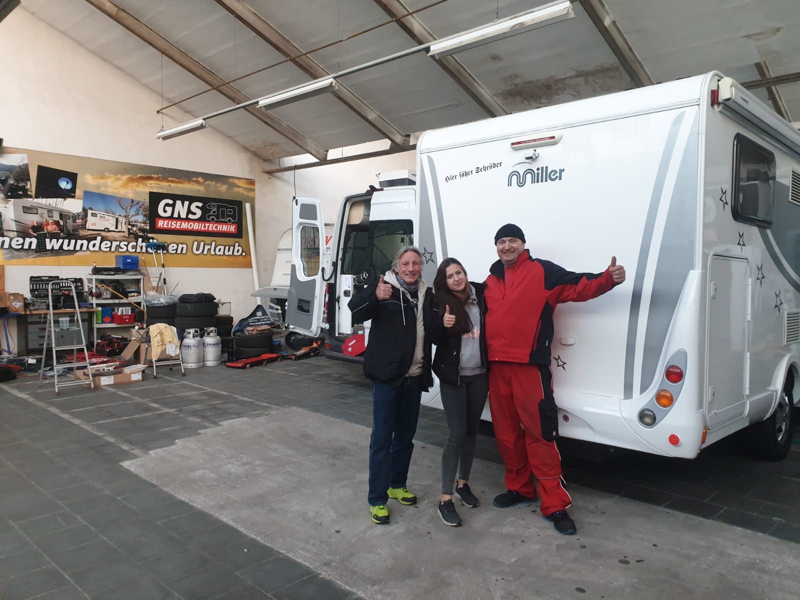 Drei Personen stehen vor einem Wohnmobil in einer Garage.