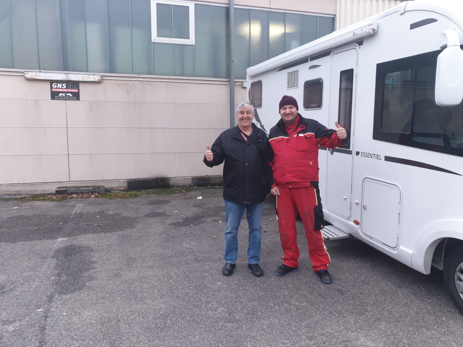 Zwei Männer stehen auf einem Parkplatz neben einem weißen Wohnmobil.