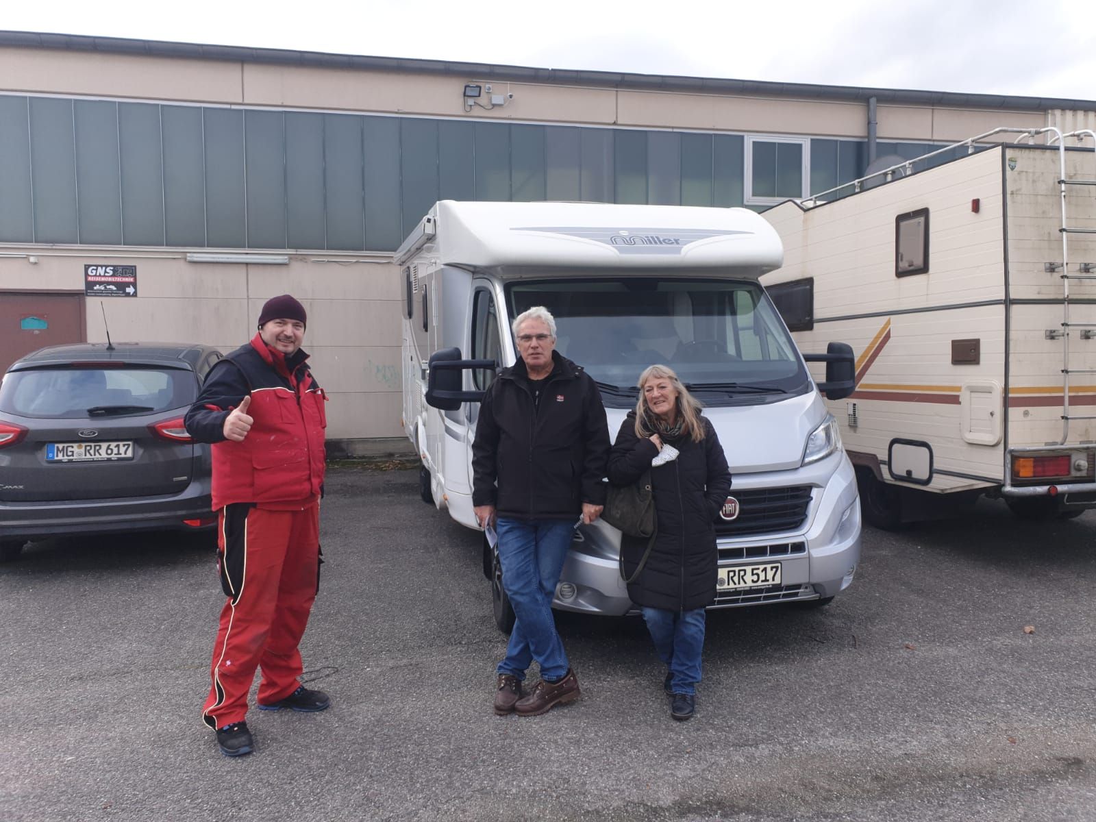 Drei Personen stehen auf einem Parkplatz vor einem Wohnmobil.