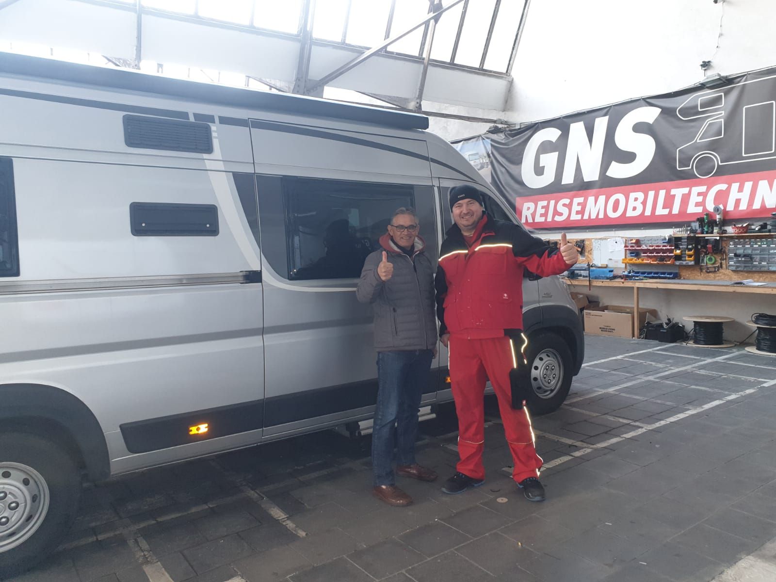 Zwei Männer stehen vor einem Lieferwagen in einer Garage.