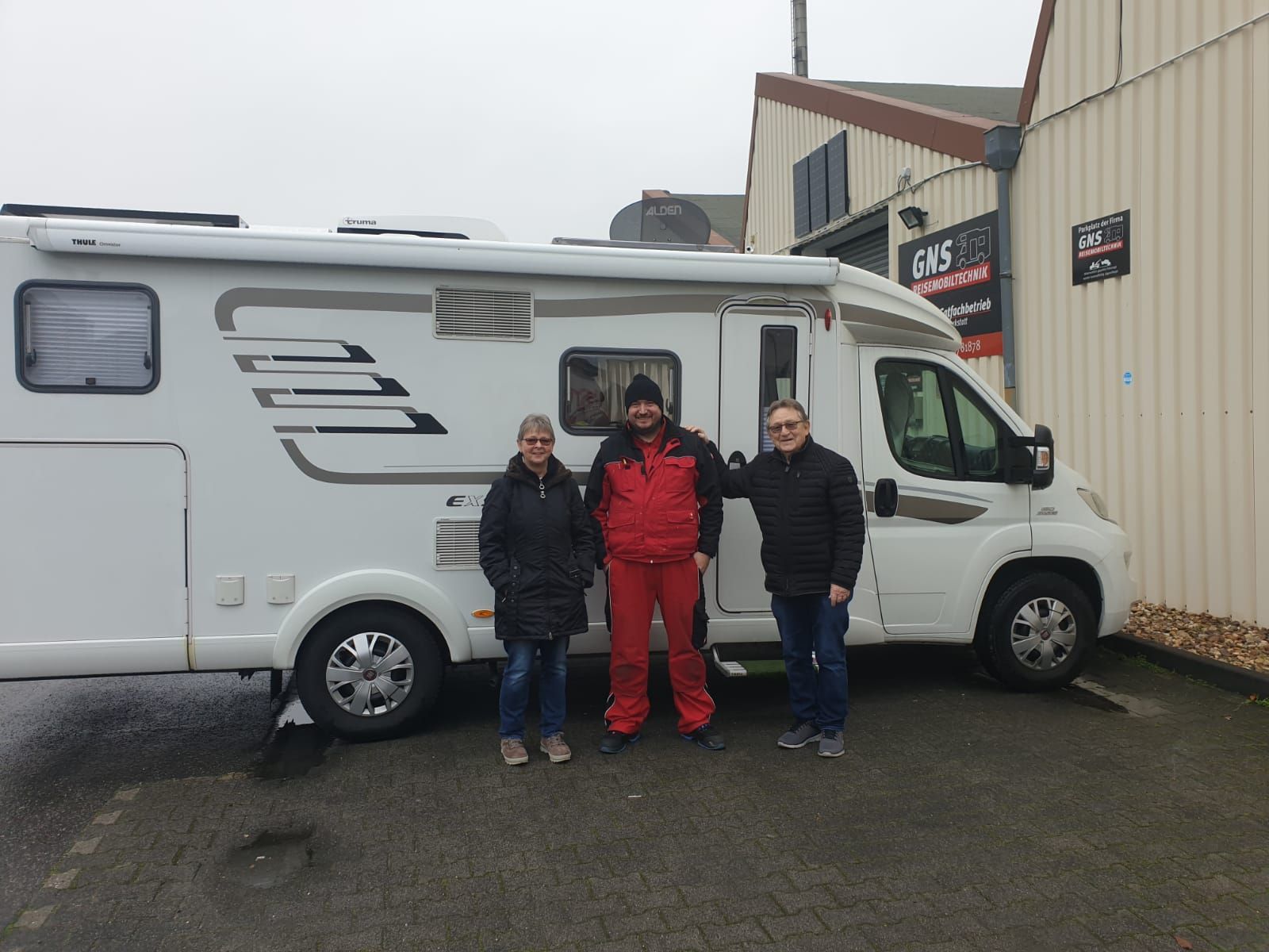 Drei Personen stehen vor einem weißen Wohnmobil.