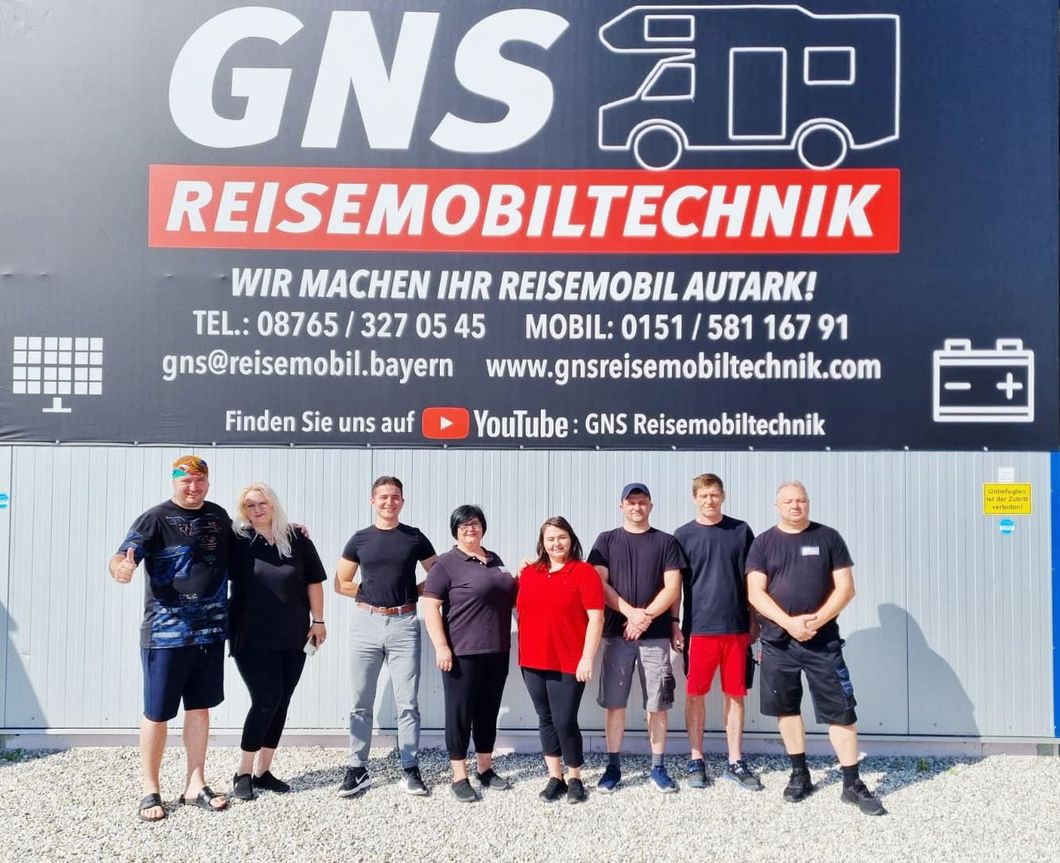 Eine Gruppe von Menschen steht vor einem Schild mit der Aufschrift „gns reisemobiltechnik“