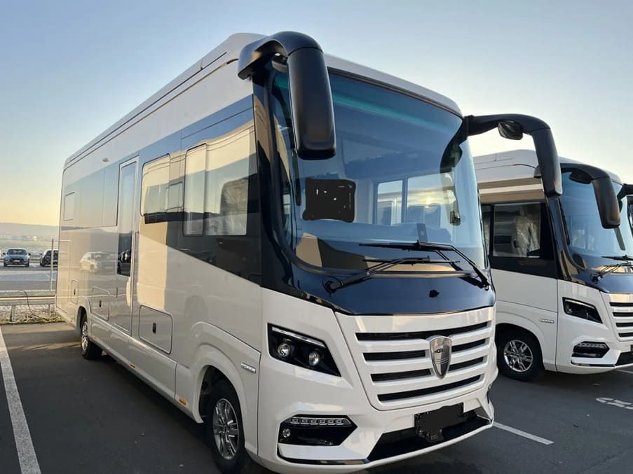 Zwei große weiße Busse stehen nebeneinander auf einem Parkplatz.