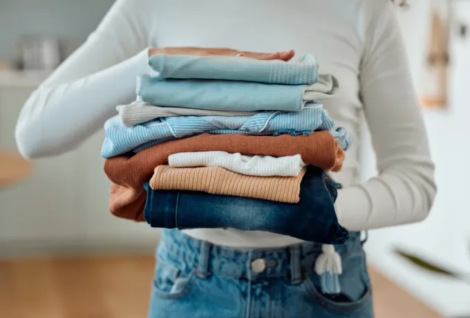 Una mujer sostiene una pila de ropa en sus manos.