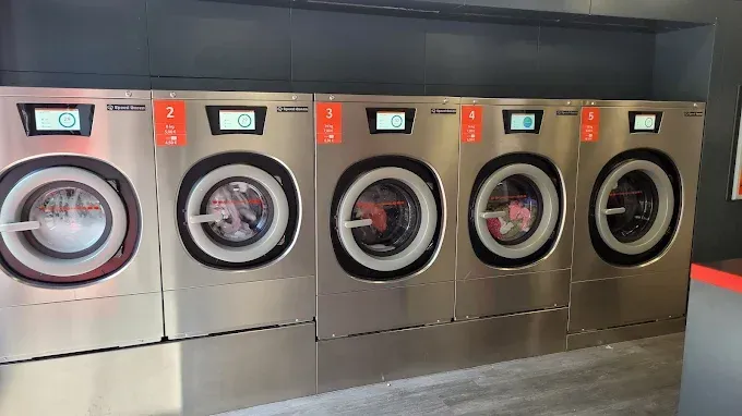Una fila de lavadoras están alineadas en una lavandería.
