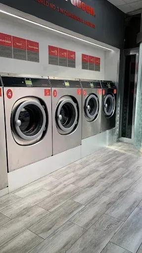 Una fila de lavadoras están alineadas en una lavandería.