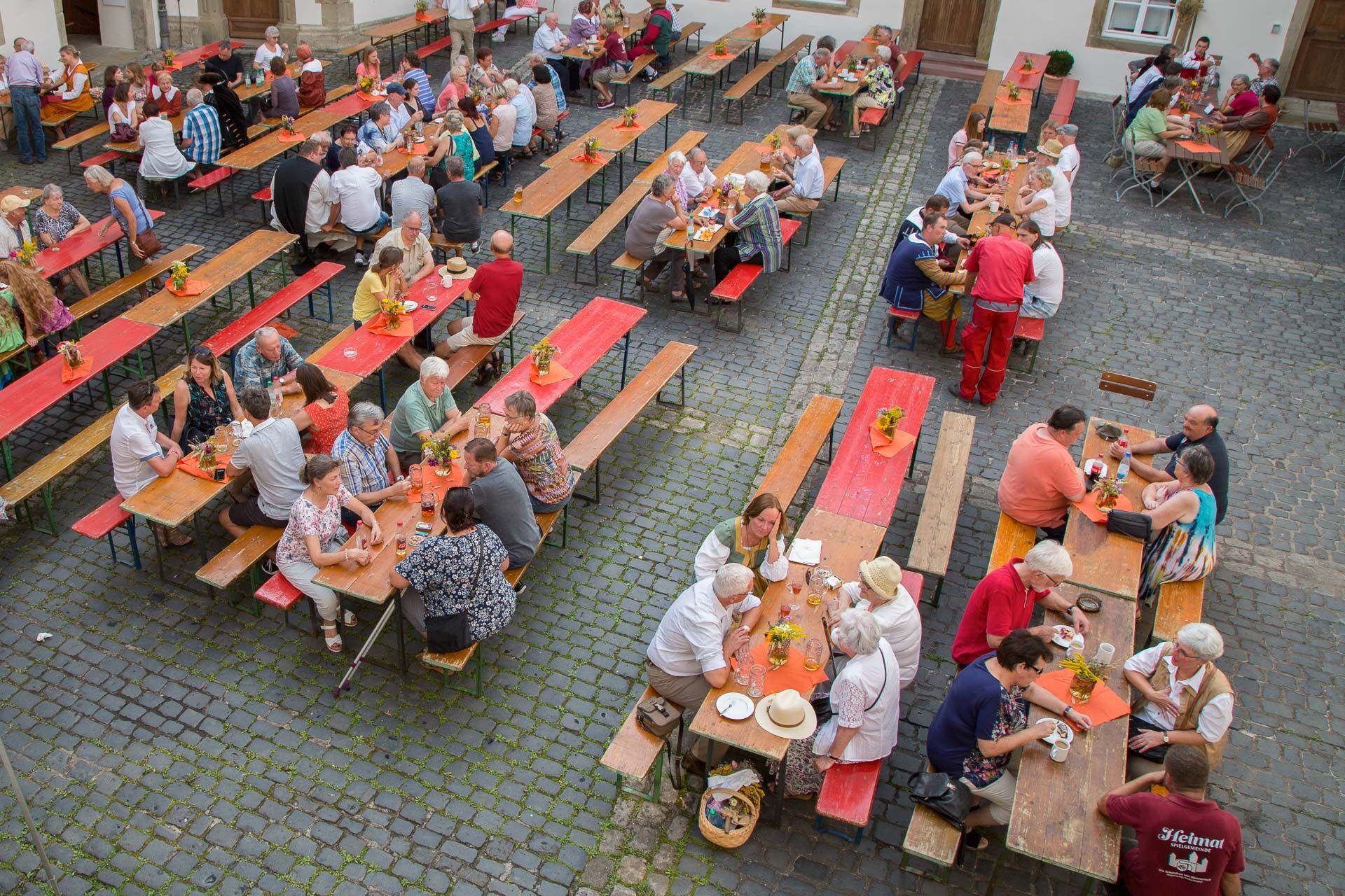 Mehrere Biertischgarnituren mit Menschen, die essen und trinken