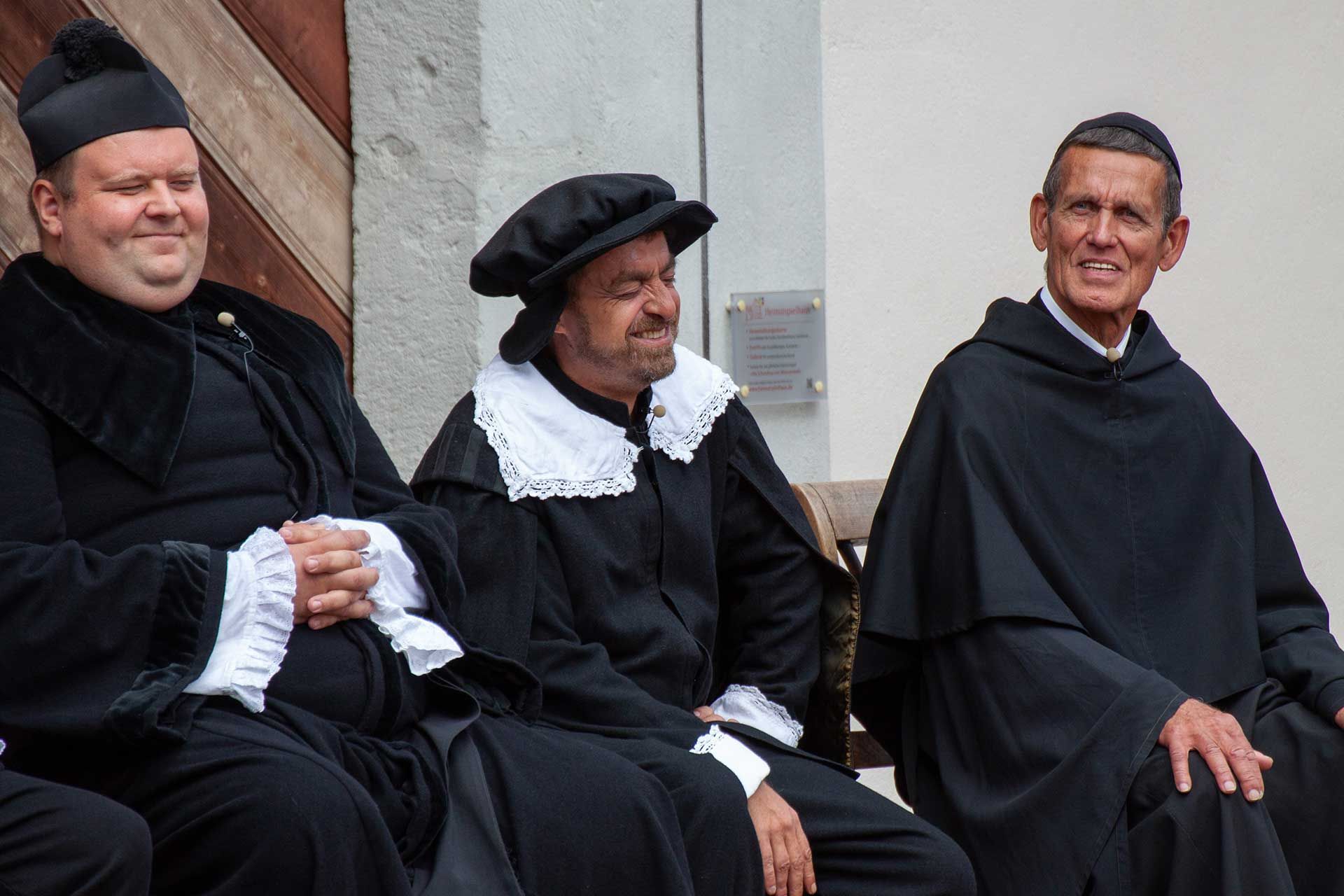 Drei Männer mit schwarzen Umhängen und weißem Kragen