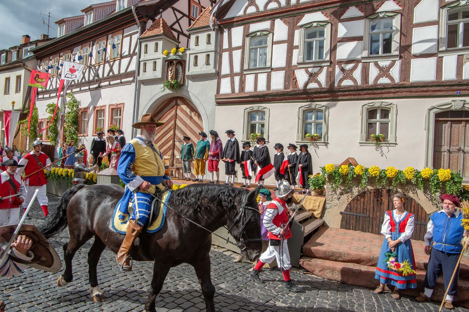 Szene aus dem Heimatspiel mit einem Reiter in blau-gelber Uniform, dahinter viele Personen in historischen Kostümen