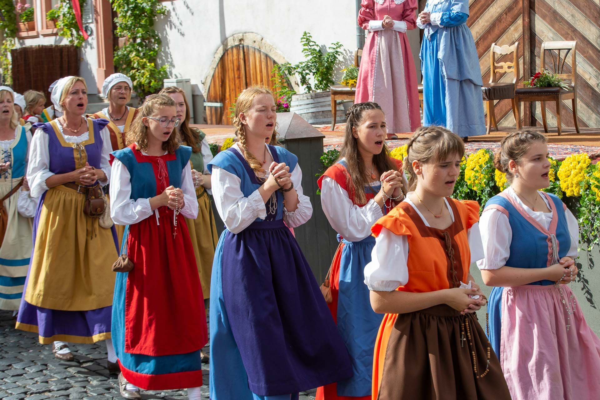 Szene aus dem Heimatspiel mit betenden Frauen in bunten Kleidern