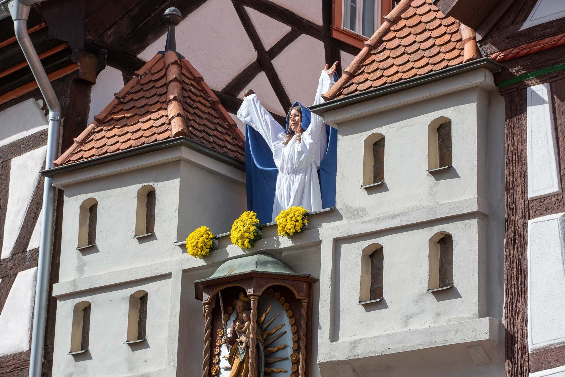 Eine Frau in weißem Kleid mit blauem Umhang steht zwischen zwei Türmen