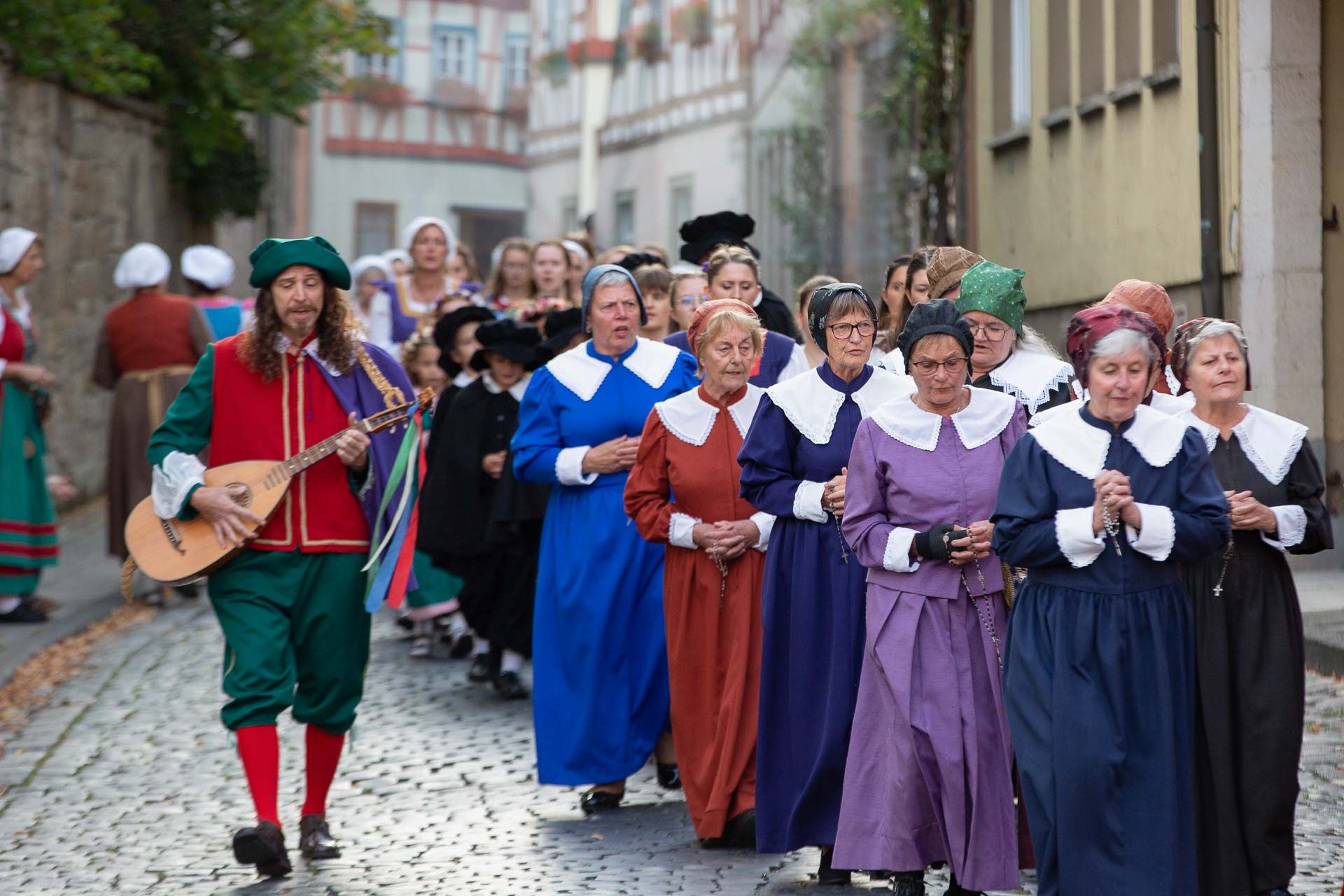 Szene aus dem Heimatspiel mit einer großen Gruppe betender Frauen und einem Musikanten