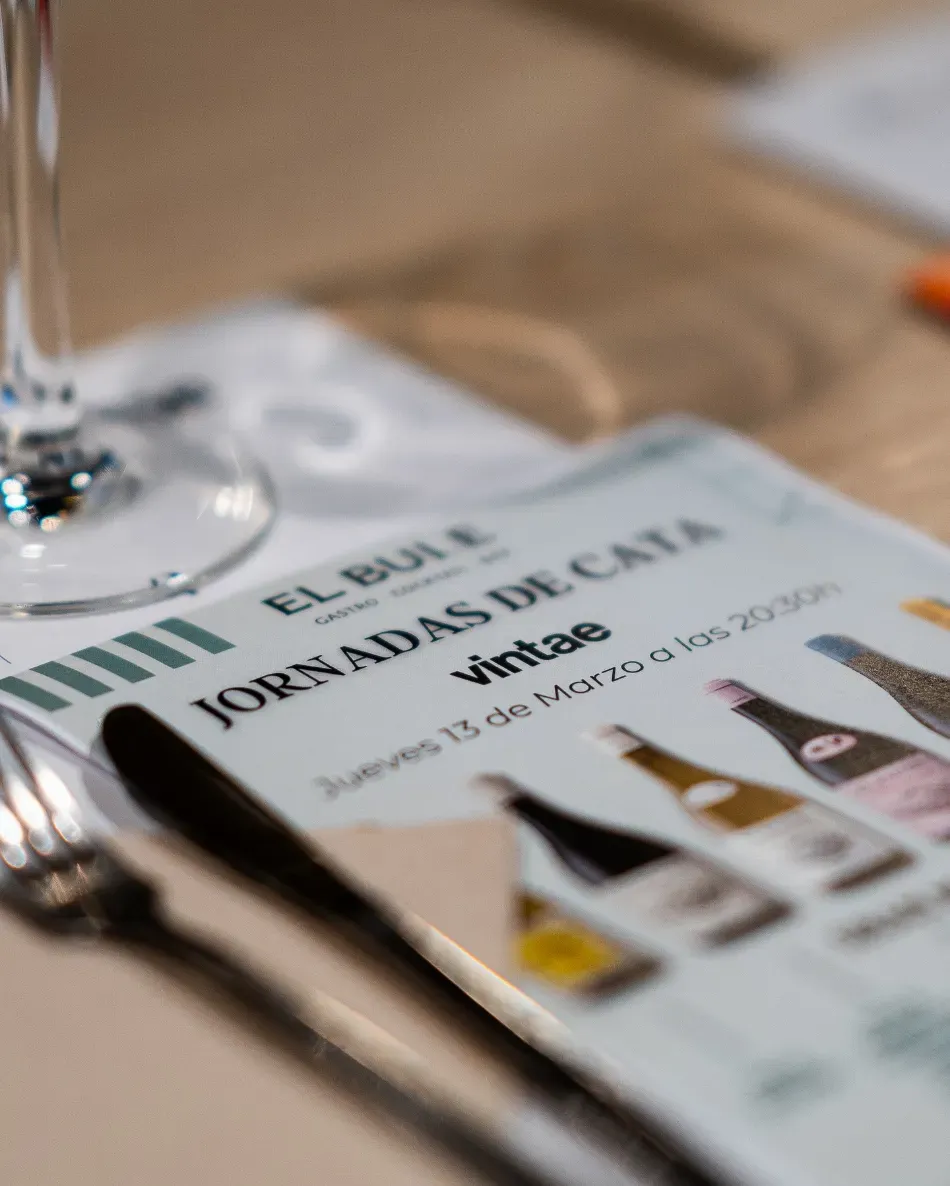 Menú sobre una mesa de madera con copas de vino, titulado “JORNADAS BUI” y “Vintage”.