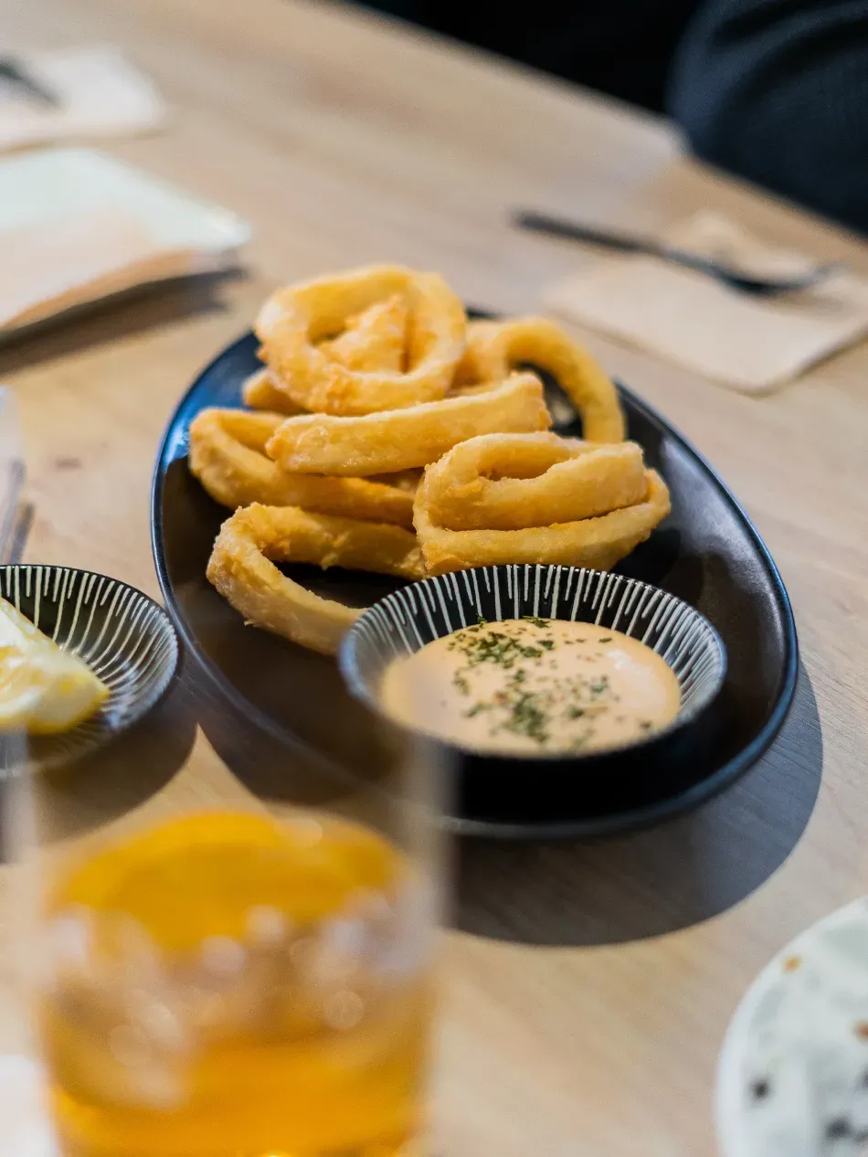 Plato de aros de cebolla fritos con salsa para mojar sobre una mesa.