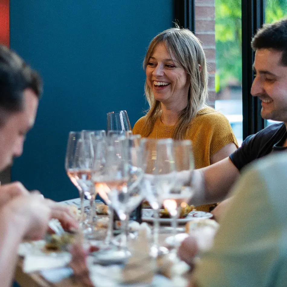 Amigos riendo juntos en una mesa de restaurante con copas de vino y platos durante la cena.