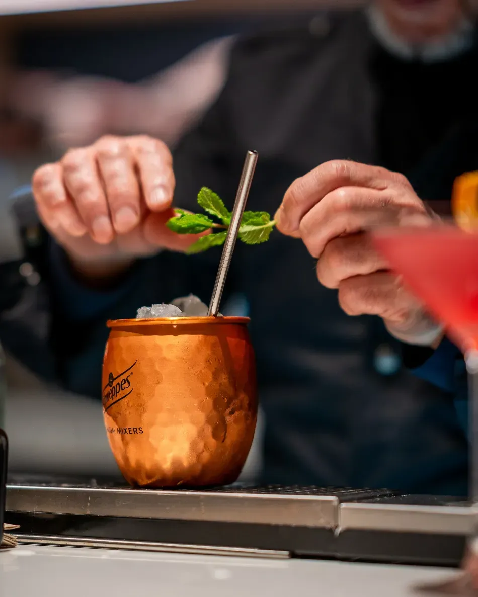 Manos preparando un cóctel de menta en una taza de cobre con una pajita en un bar.