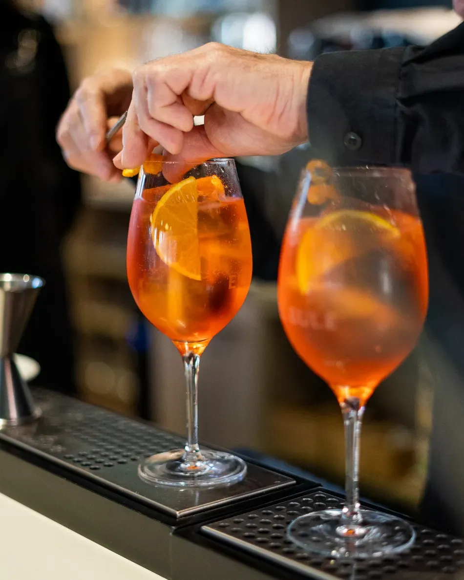 Un camarero decora dos cócteles de naranja con rodajas de naranja en un bar.