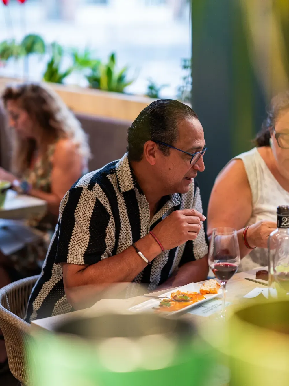 Mujer con una camisa de rayas blancas y negras comiendo en una mesa de un restaurante, con bebidas y platos cerca.