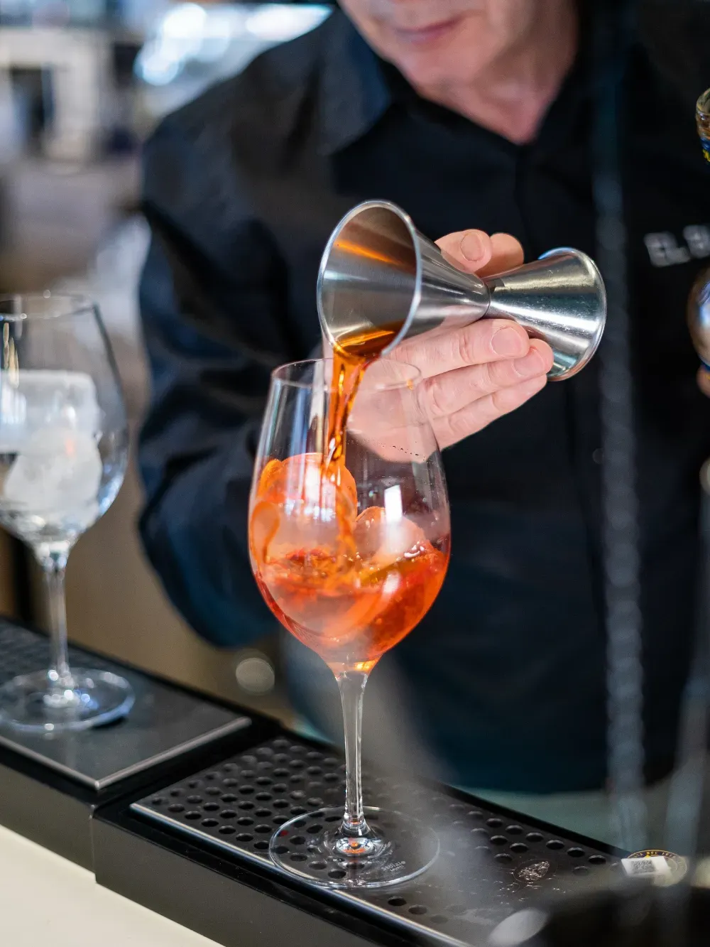 Un camarero sirve un cóctel de naranja en una copa de vino en un bar.