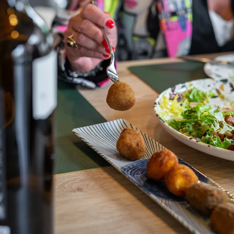 Levantando con un tenedor un aperitivo frito junto a un plato de ensalada y una hilera de croquetas.