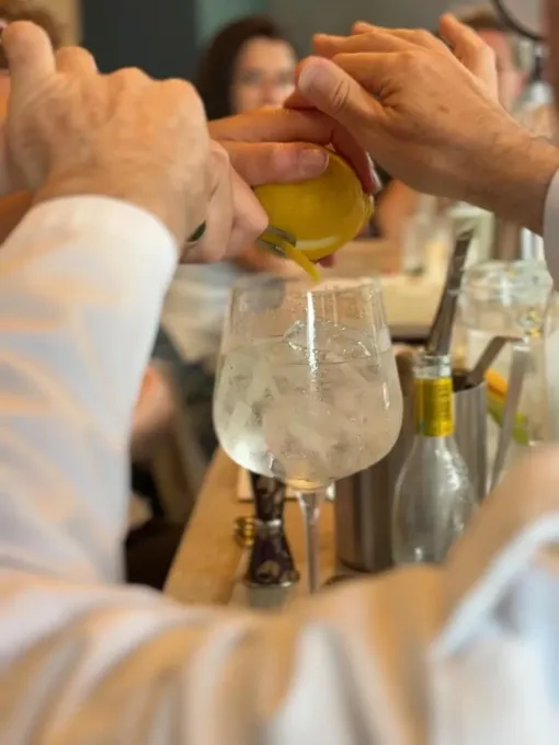 Unas manos vierten una bebida amarilla en un vaso grande lleno de hielo en una mesa.