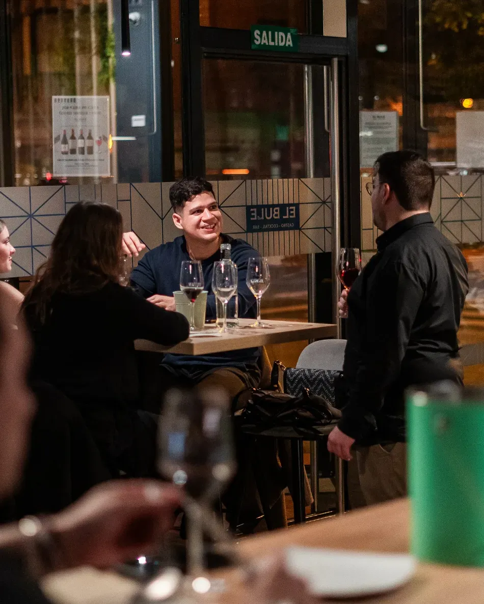 Gente sentada en una mesita en un bar o cafetería con iluminación cálida, charlando mientras toman algo por la noche.