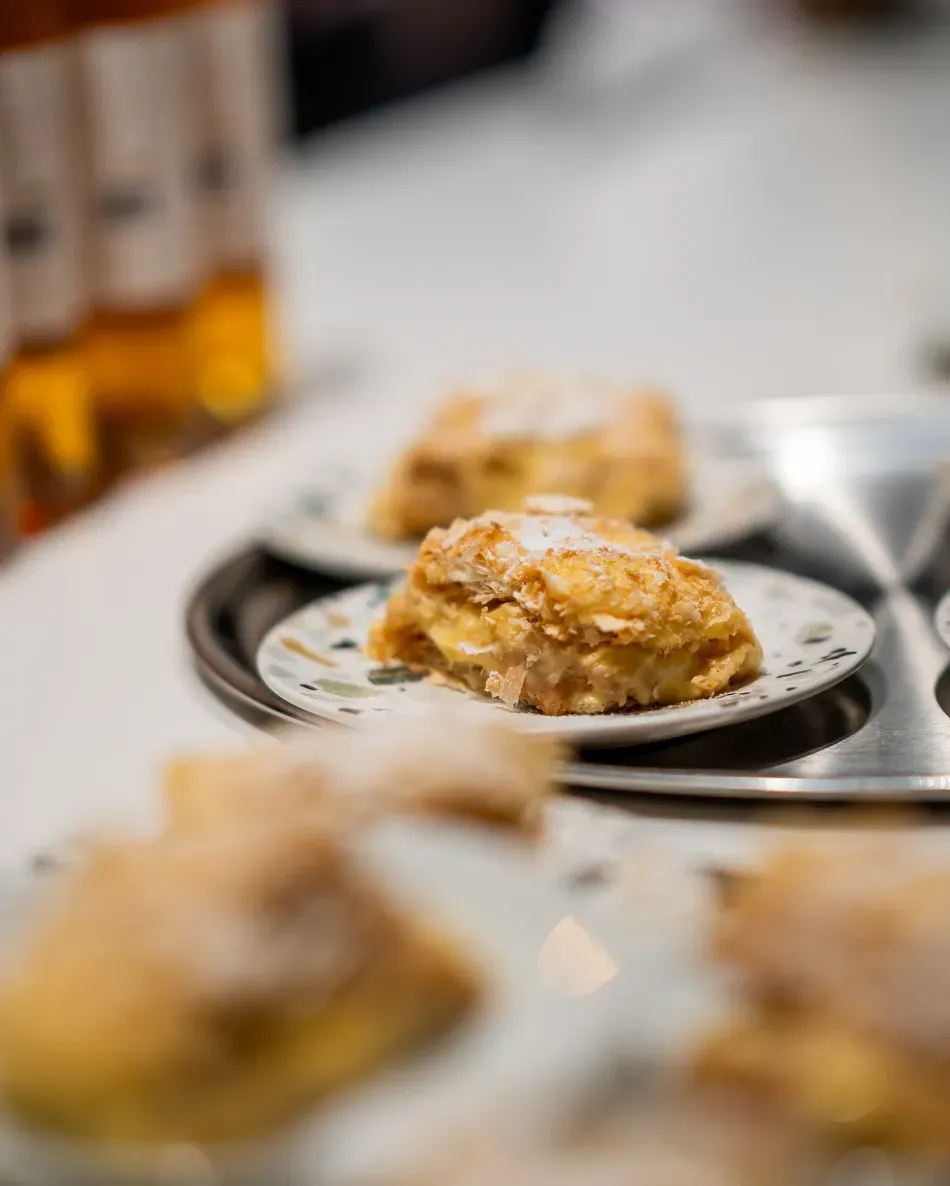 Plato de bocaditos de hojaldre dorados sobre una mesa, con copas de vino borrosas al fondo.