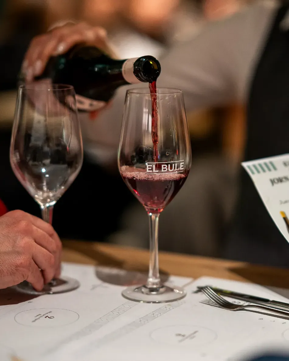 Persona sirviendo vino tinto en una copa en la mesa de un restaurante.