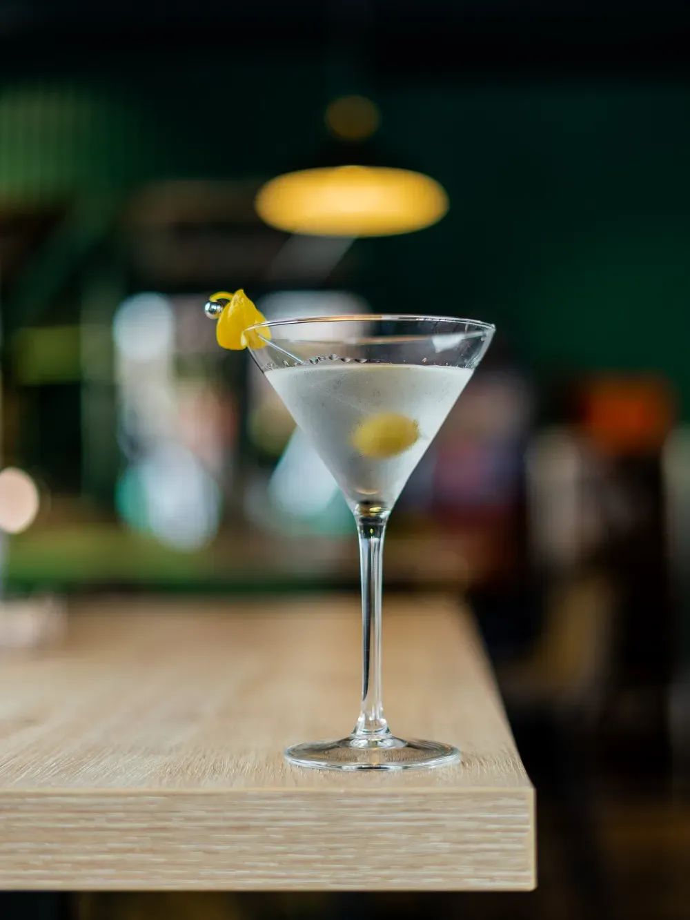 Una copa de martini con una rodaja de limón sobre una mesa de madera en un bar con luz tenue.