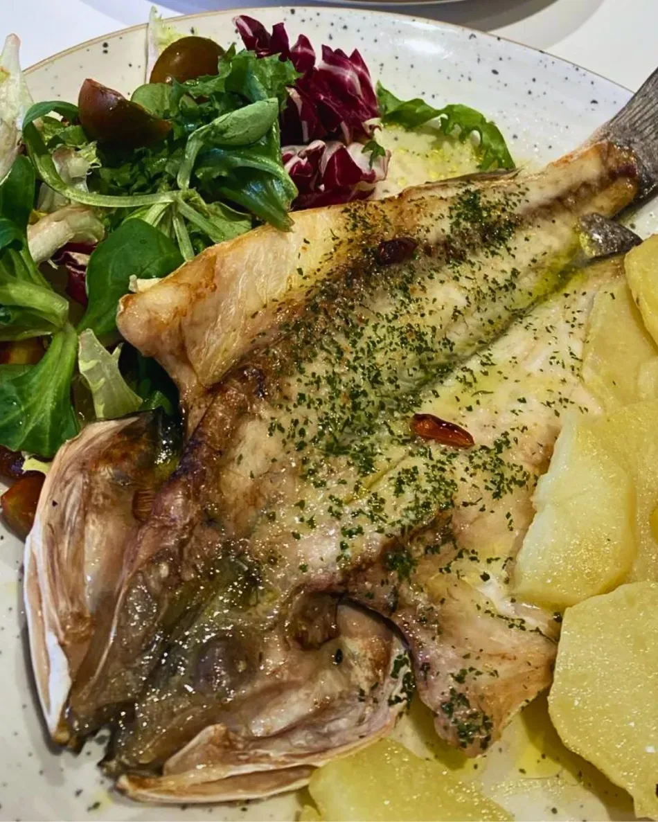 Pescado al horno con hierbas, acompañado de patatas y verduras variadas en un plato blanco.