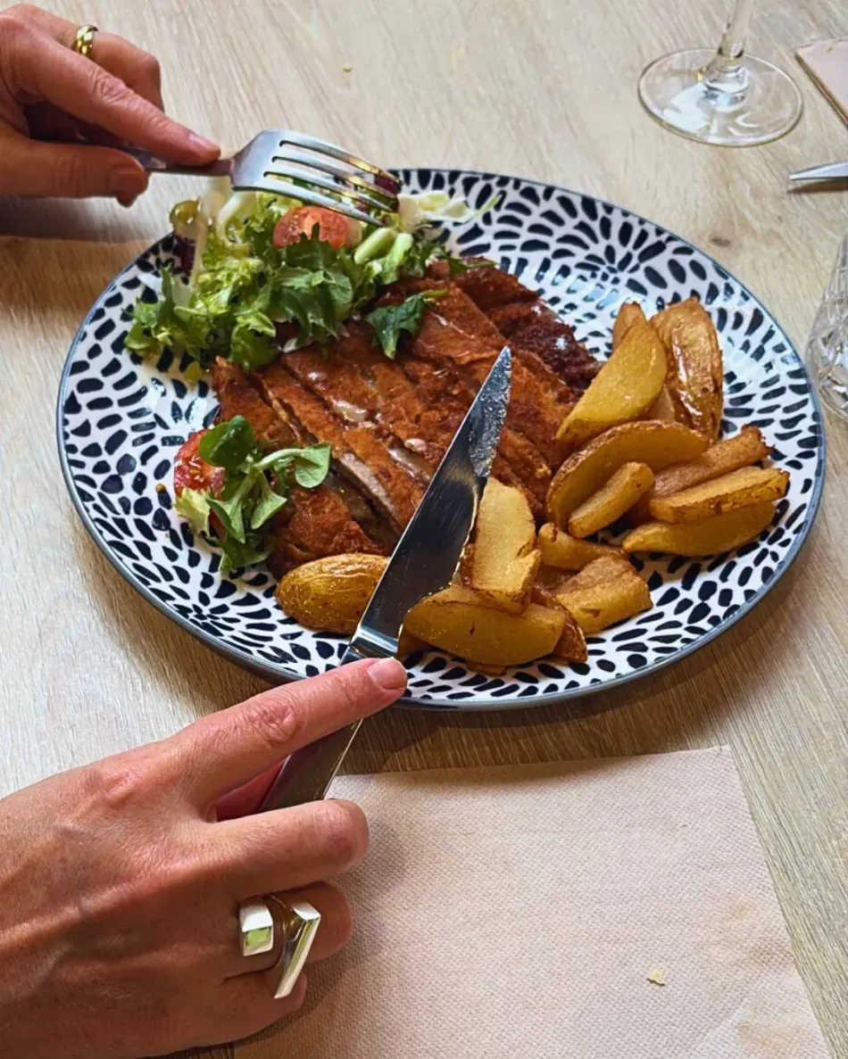 Manos cortando un plato con ensalada y patatas gajo sobre un plato estampado.