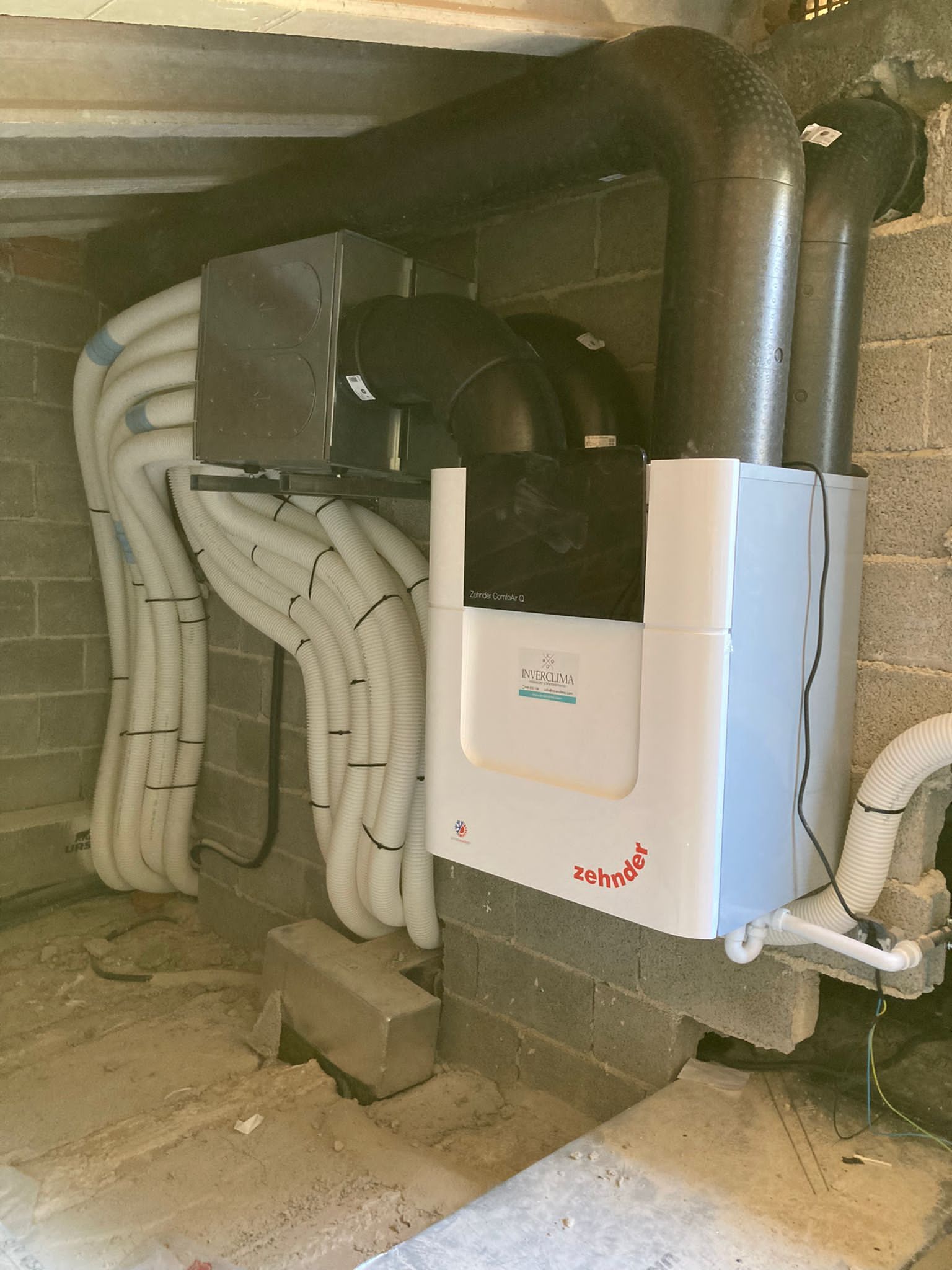 Una caja blanca está sobre una pared de ladrillos al lado de un montón de tuberías.