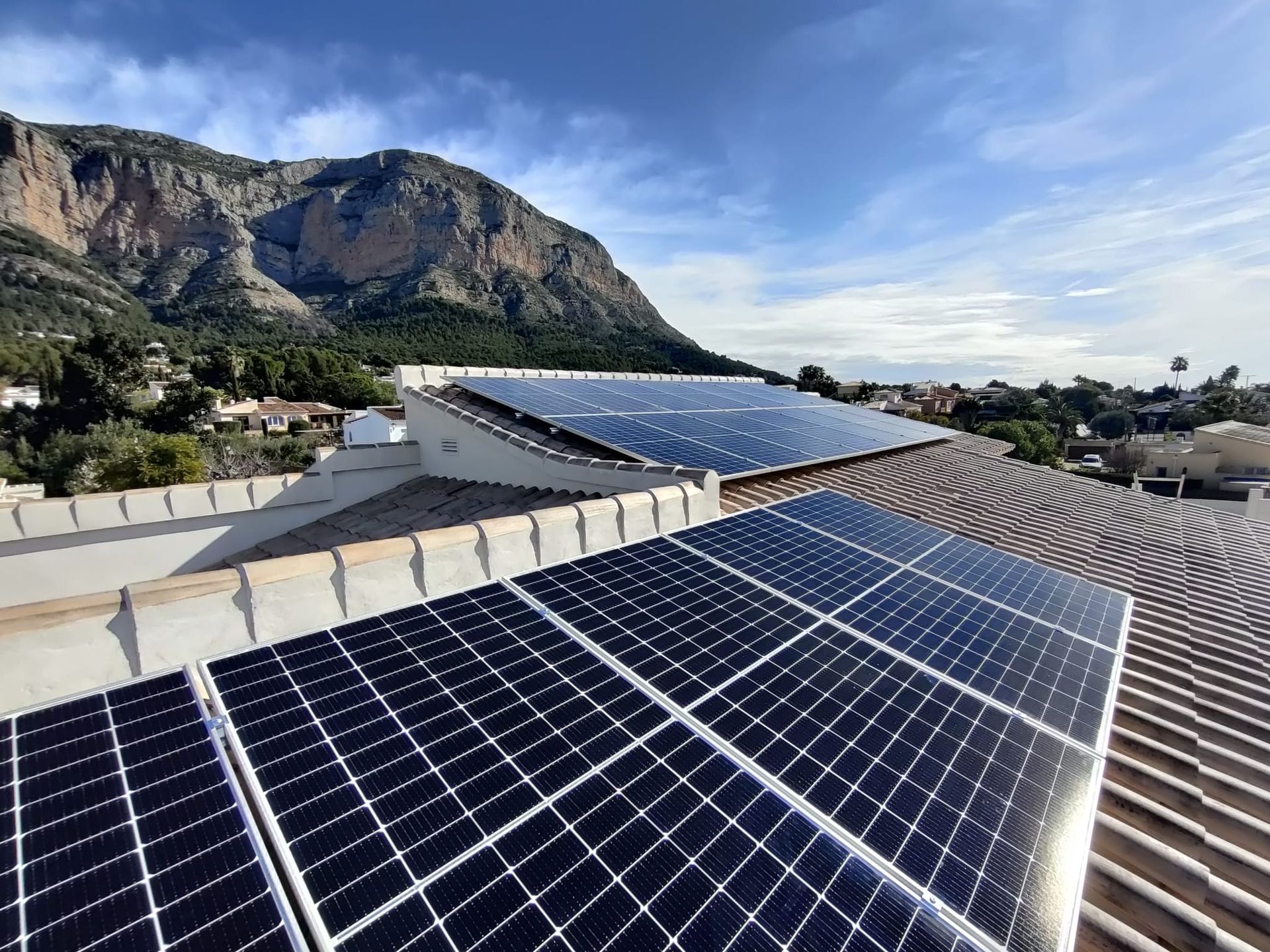 Un montón de paneles solares en un tejado con montañas al fondo.