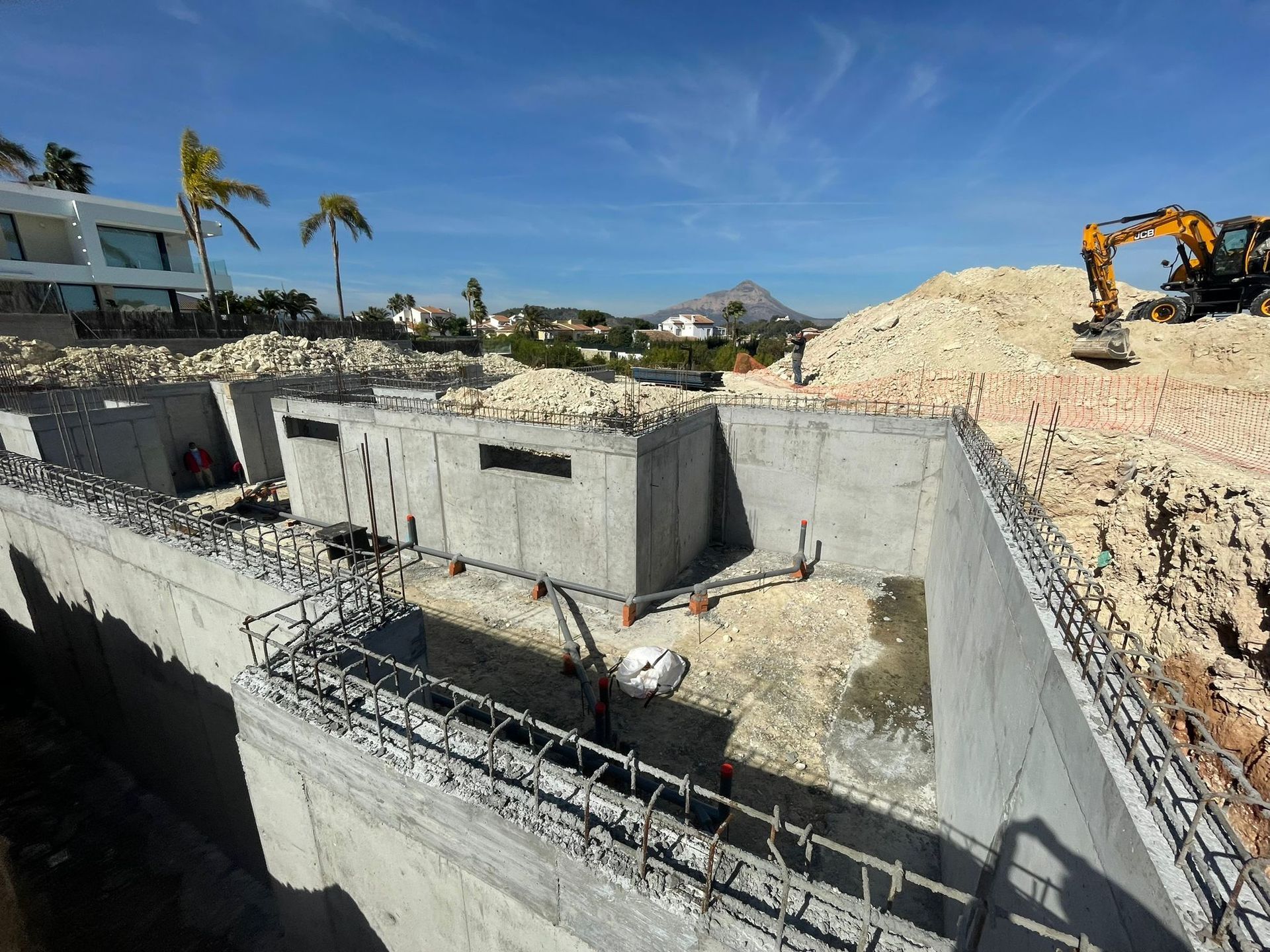 Se está construyendo una gran estructura de hormigón con una excavadora al fondo.