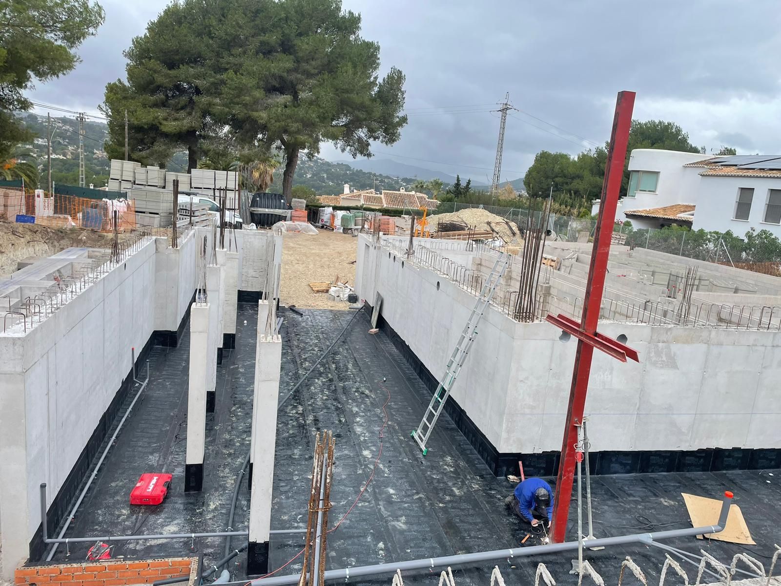 Una obra en construcción con un gran muro de hormigón y un poste rojo en primer plano.