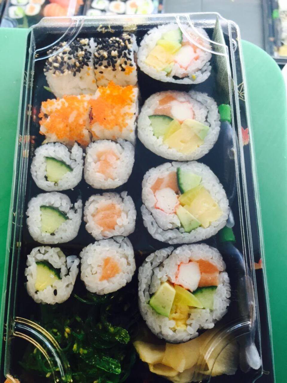 Plateau de sushis dans un récipient en plastique noir, présentant différents rouleaux de poisson et de légumes.