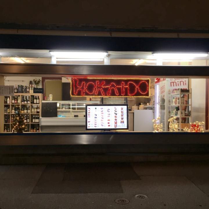 La nuit, une devanture de magasin éclairée par des néons. L'enseigne indique « HOKAHDO ». Un menu est affiché devant.