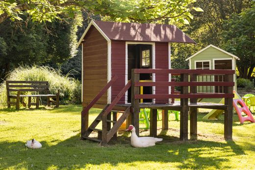 Des bâtiments en pierre aux toits de tuiles rouges nichés parmi les arbres, une pelouse verdoyante avec une maisonnette et un jardin.