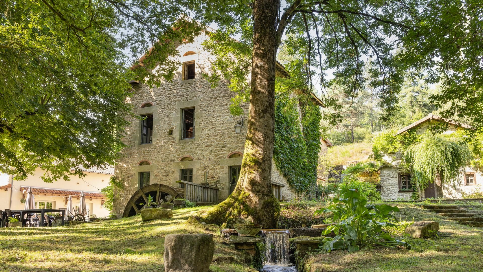 Moulin à eau en pierre avec roue à aubes en bois, niché dans un paysage verdoyant luxuriant.