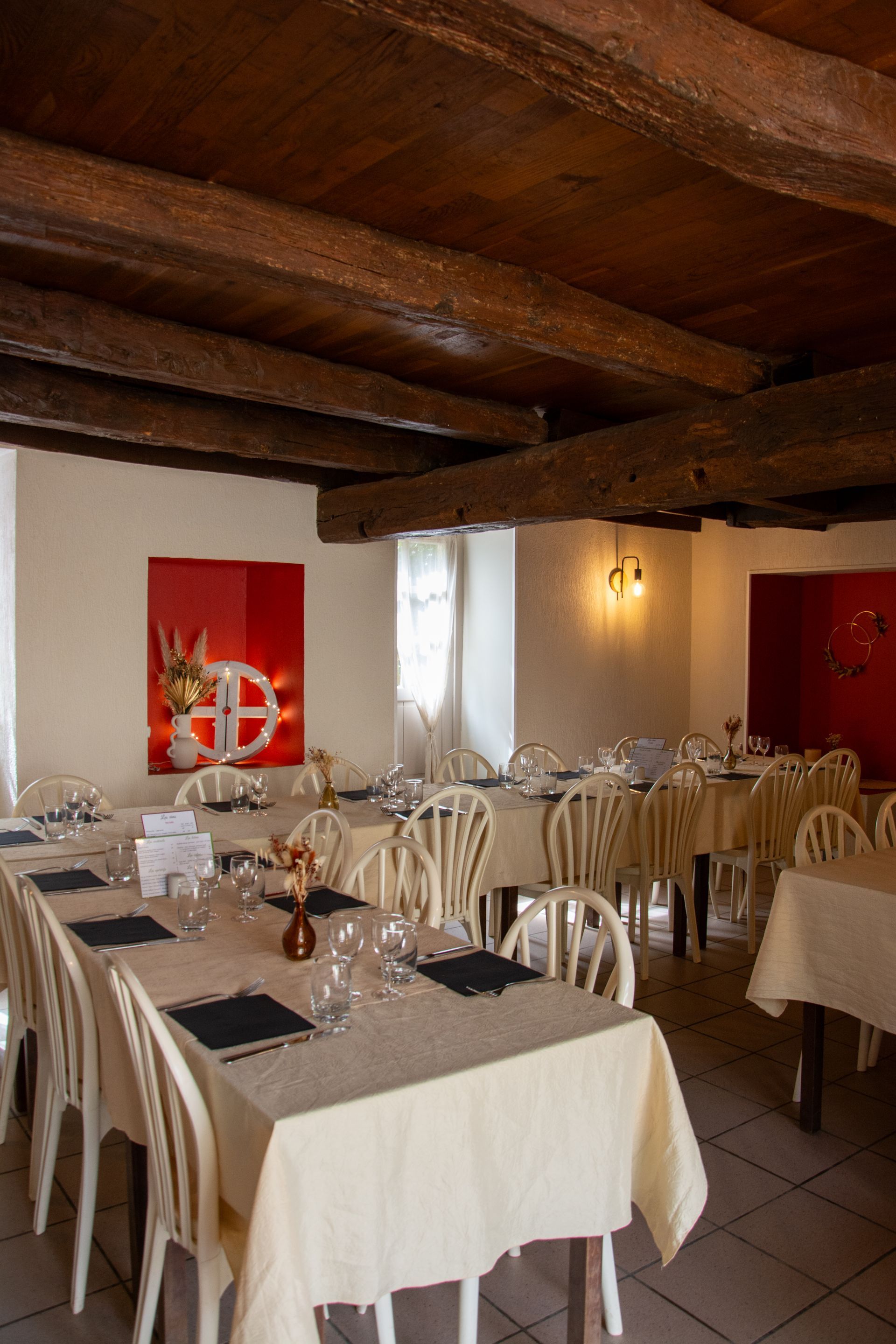 Salle à manger du restaurant avec tables et chaises blanches, poutres en bois et œuvres d'art aux murs.