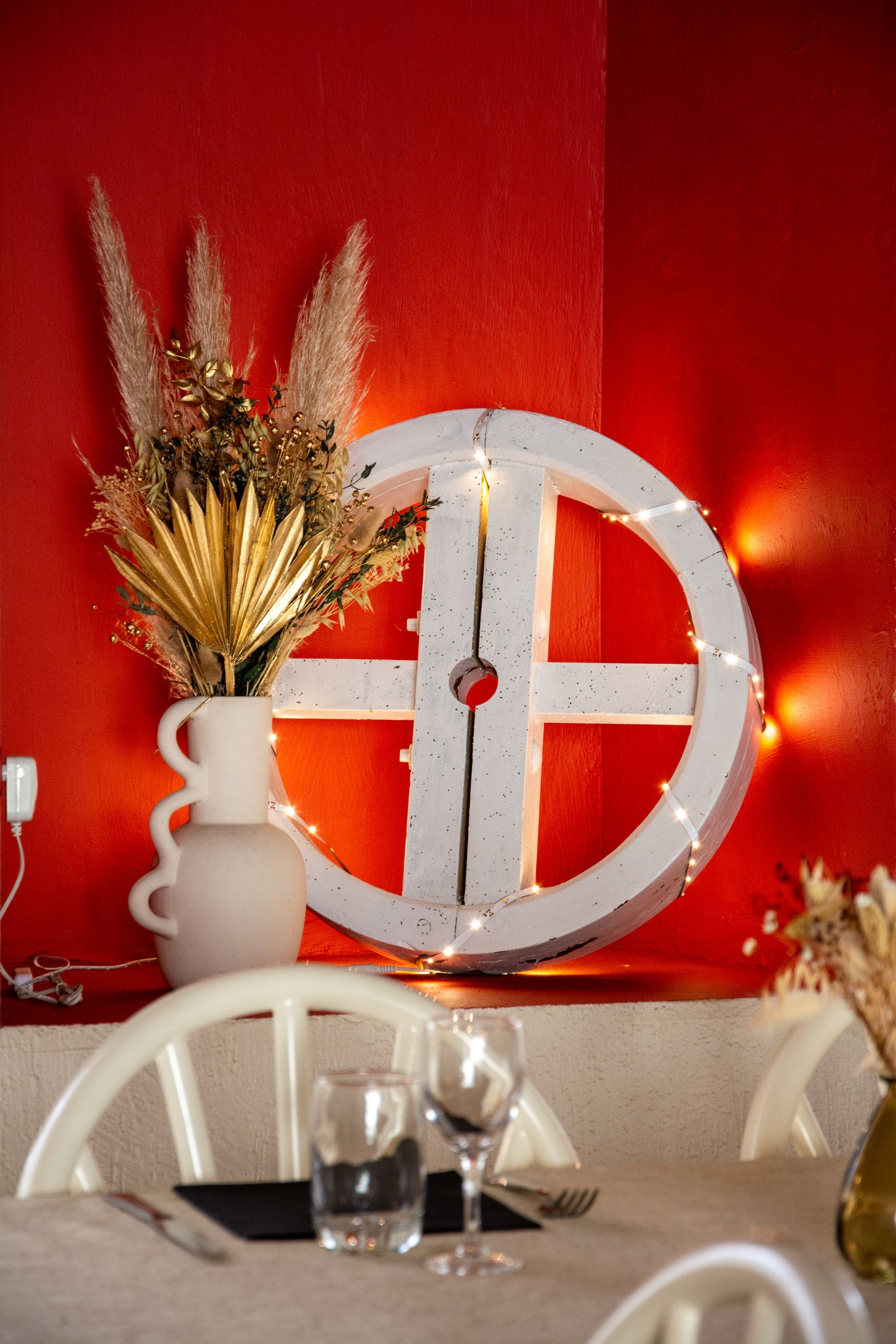 Décoration blanche en forme de roue avec guirlande lumineuse sur un mur rouge, avec table à manger et vase.