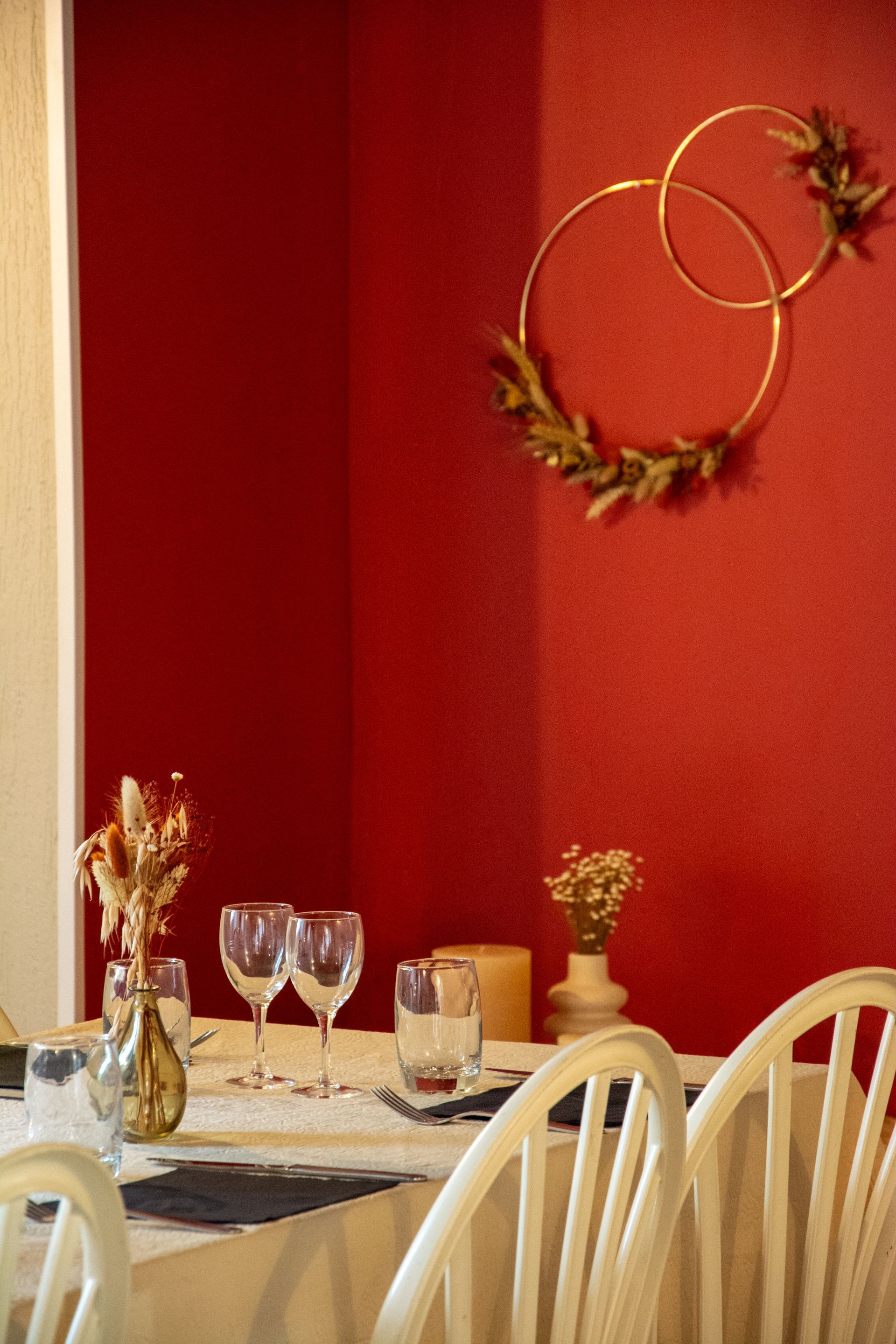 Table à manger dressée pour un repas dans une pièce aux murs rouges, ornée de cerceaux dorés et de chaises blanches.