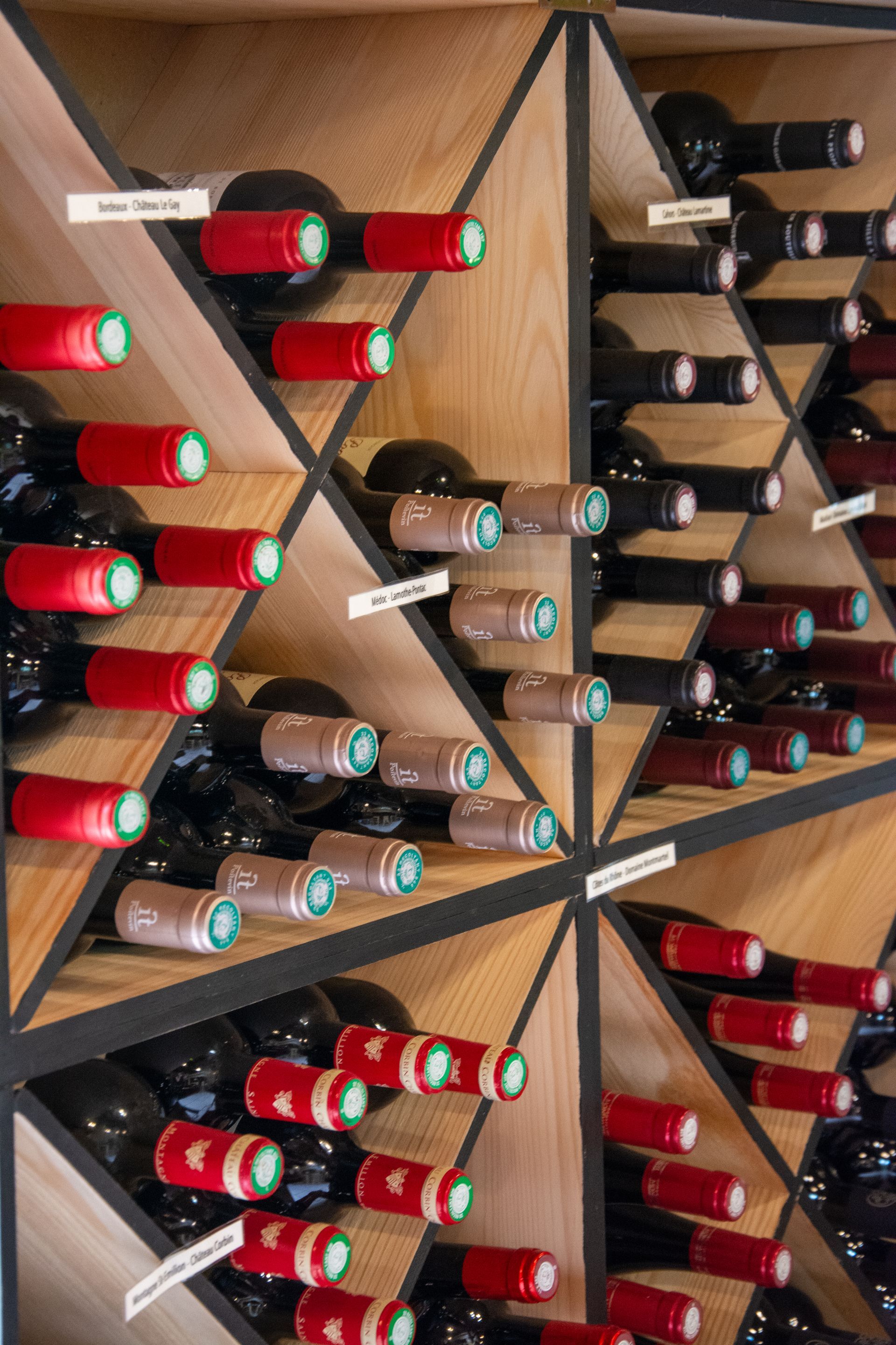 Bouteilles de vin dans des compartiments de rangement en bois en forme de losange, avec des étiquettes rouges et brunes.