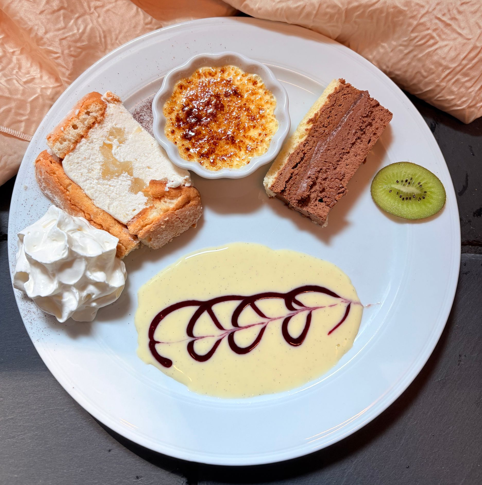 Tranche de clafoutis aux cerises avec crème fouettée et sauce, garnie de menthe et de kiwi.