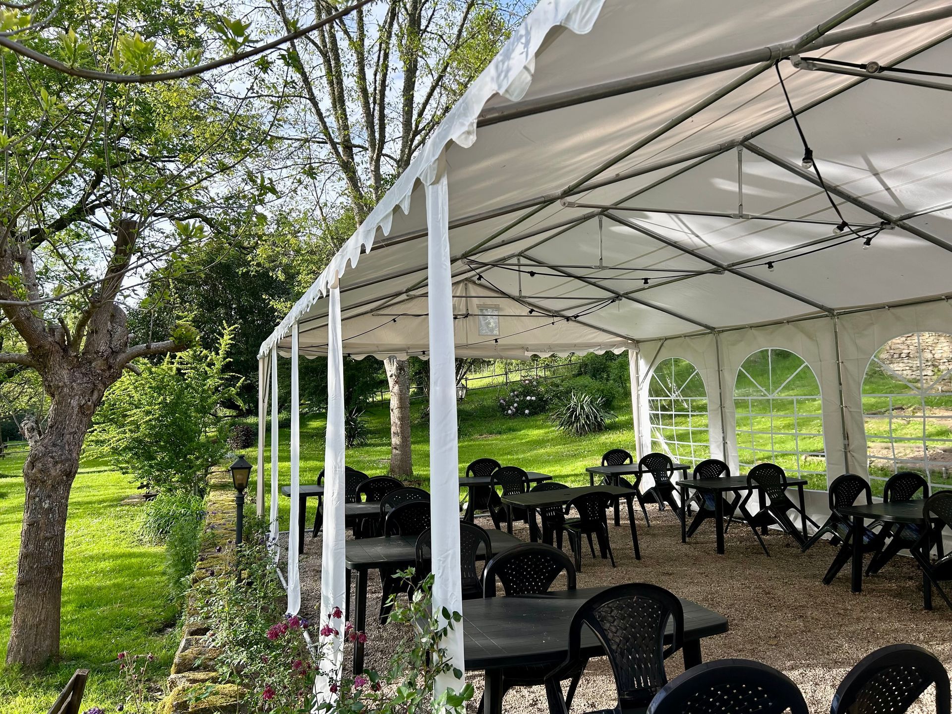 Des bâtiments en pierre aux toits de tuiles rouges nichés parmi les arbres, une pelouse verdoyante avec une maisonnette et un jardin.