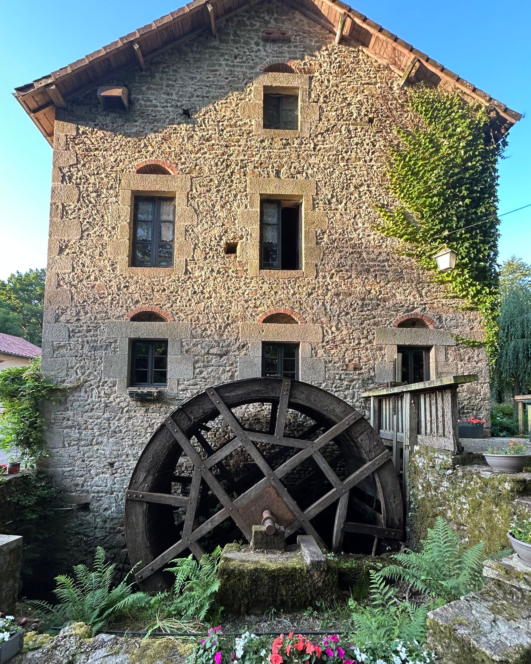 Roue à eau d'un ancien moulin en pierre, avec fenêtres, porte et petit coin salon extérieur.