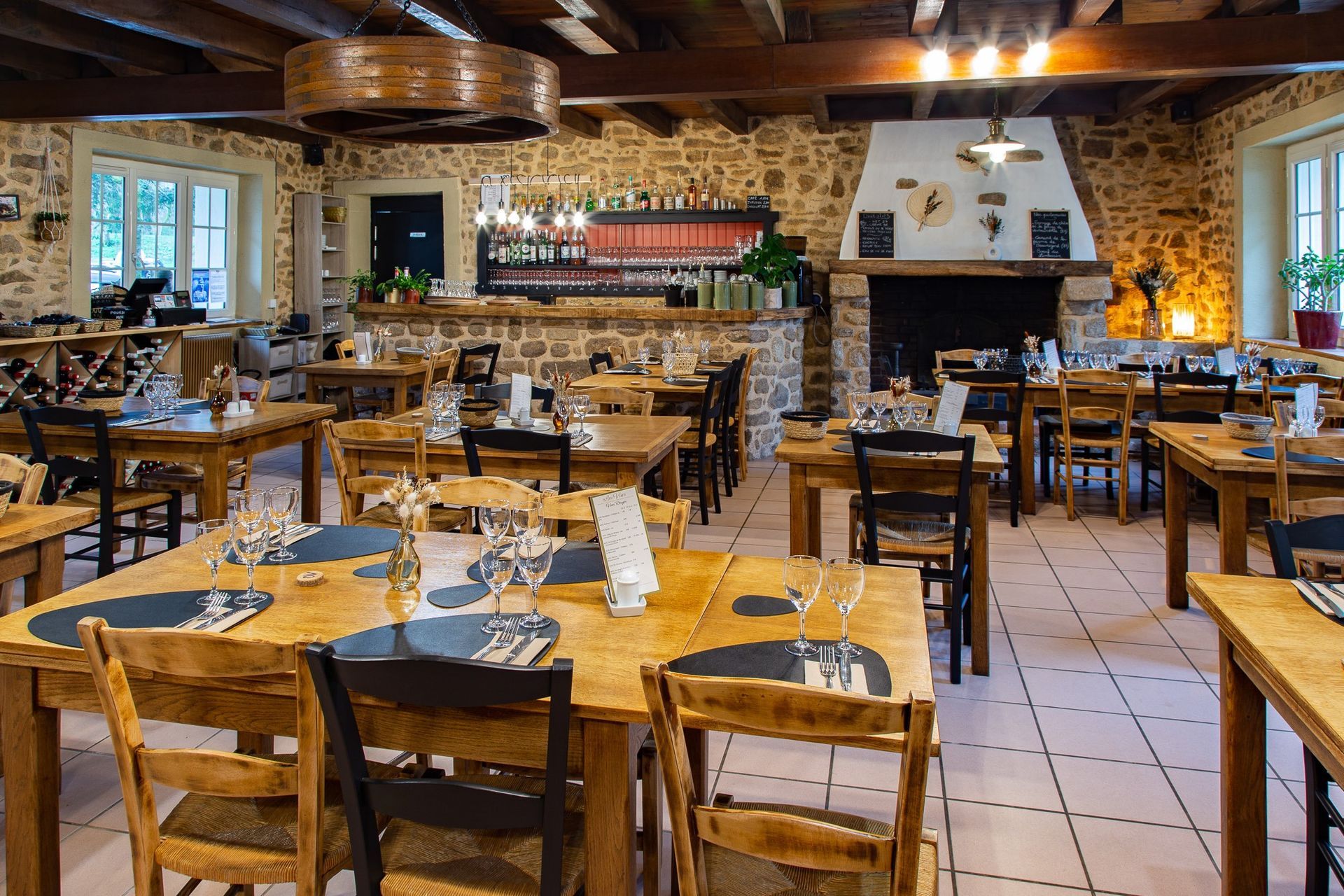Intérieur du restaurant : tables et chaises en bois, murs en pierre, bar, cheminée.