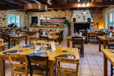 Intérieur du restaurant : tables et chaises en bois, murs en pierre, bar, cheminée.