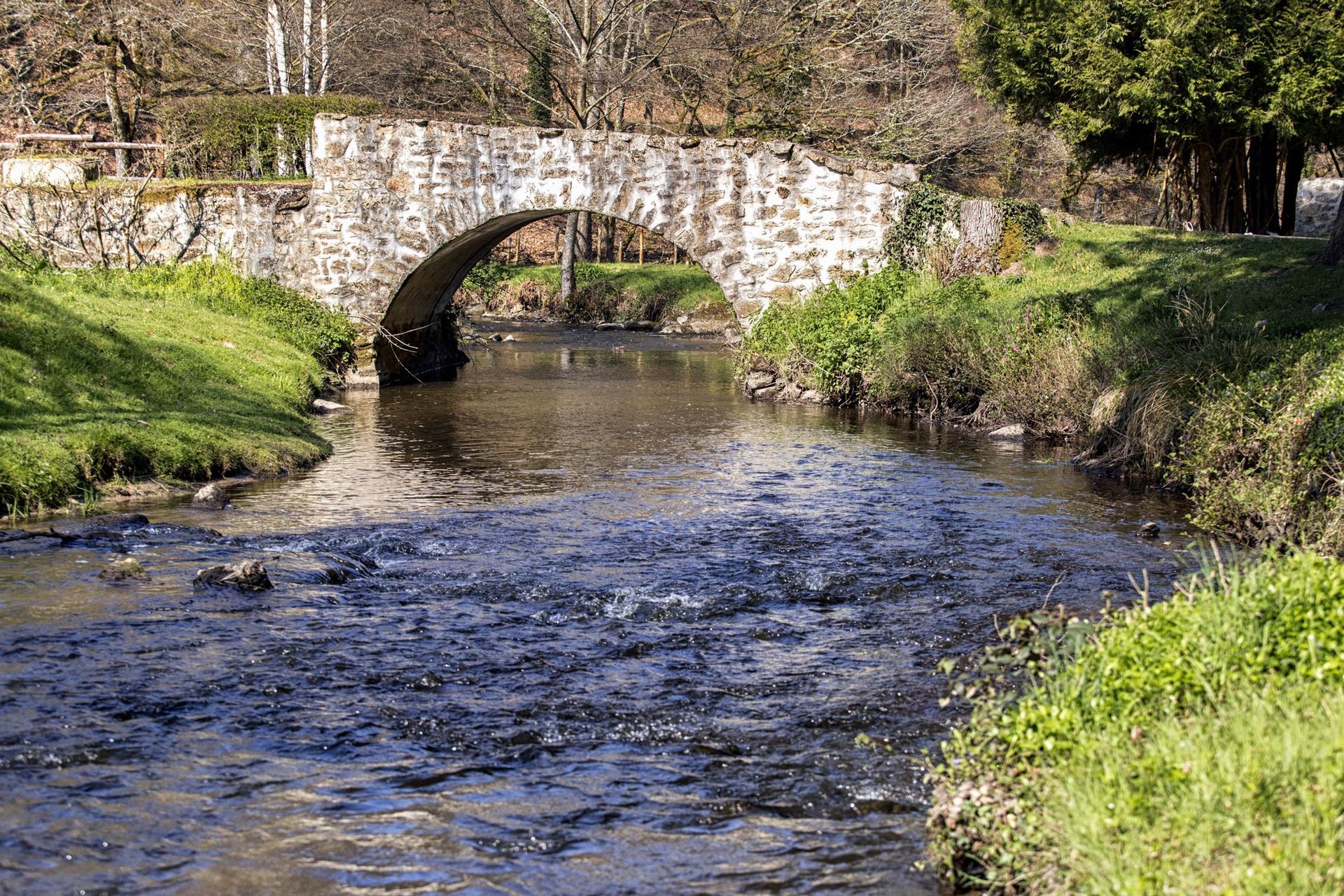 Pont de pierre enjambant une rivière. L'herbe verte borde les berges ; des arbres se dressent à l'arrière-plan.